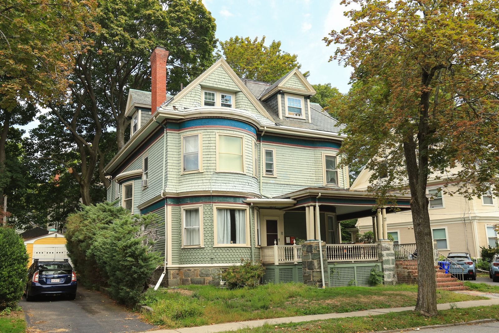 Classic two-story Victorian home with a covered porch, steep shingle roof, and mature trees