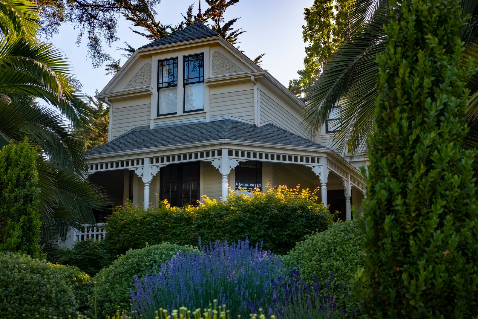 Victorian-style home with steep rooflines surrounded by a lush garden
