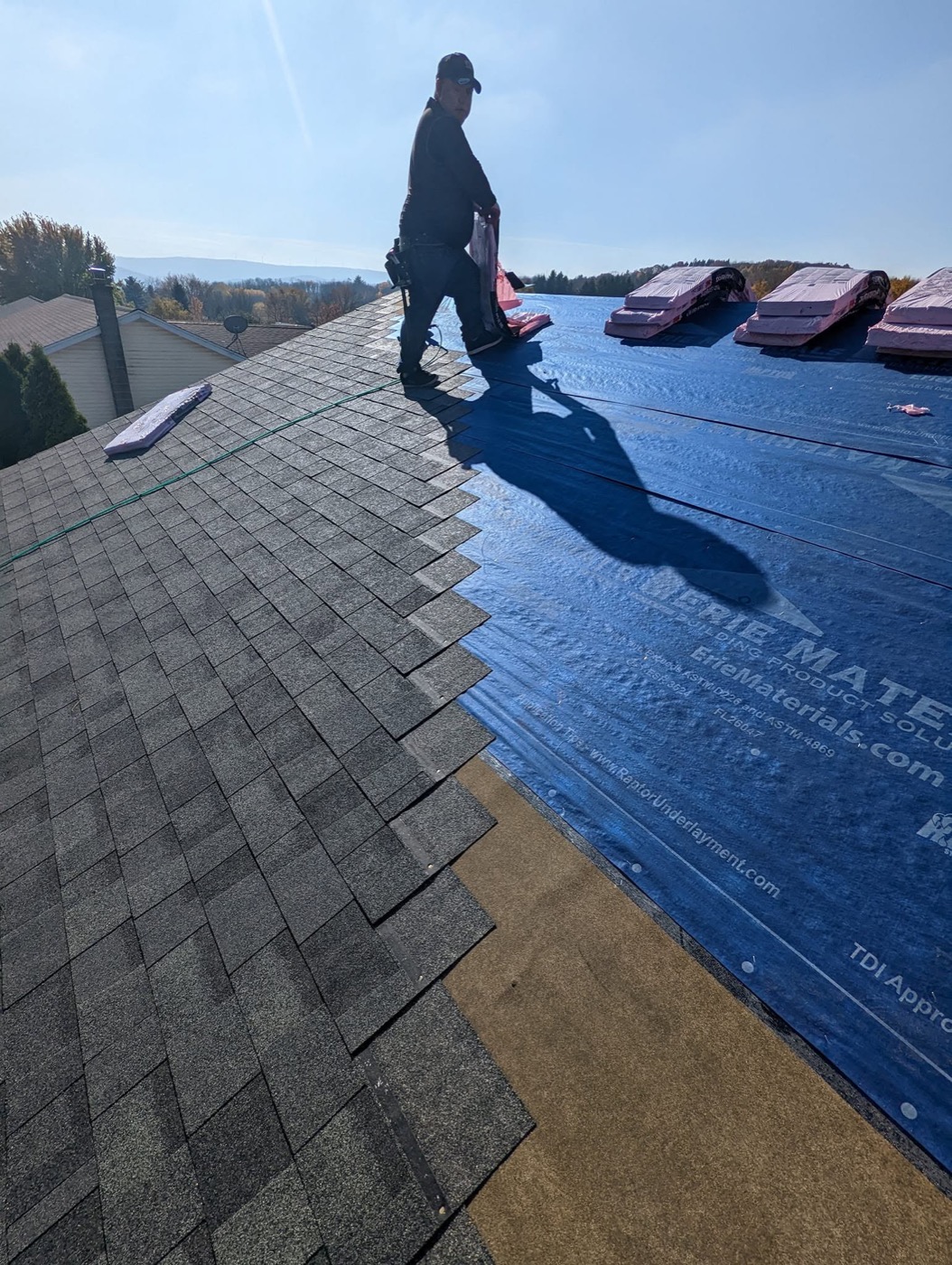 Crew rolling out synthetic underlayment across a long roof deck