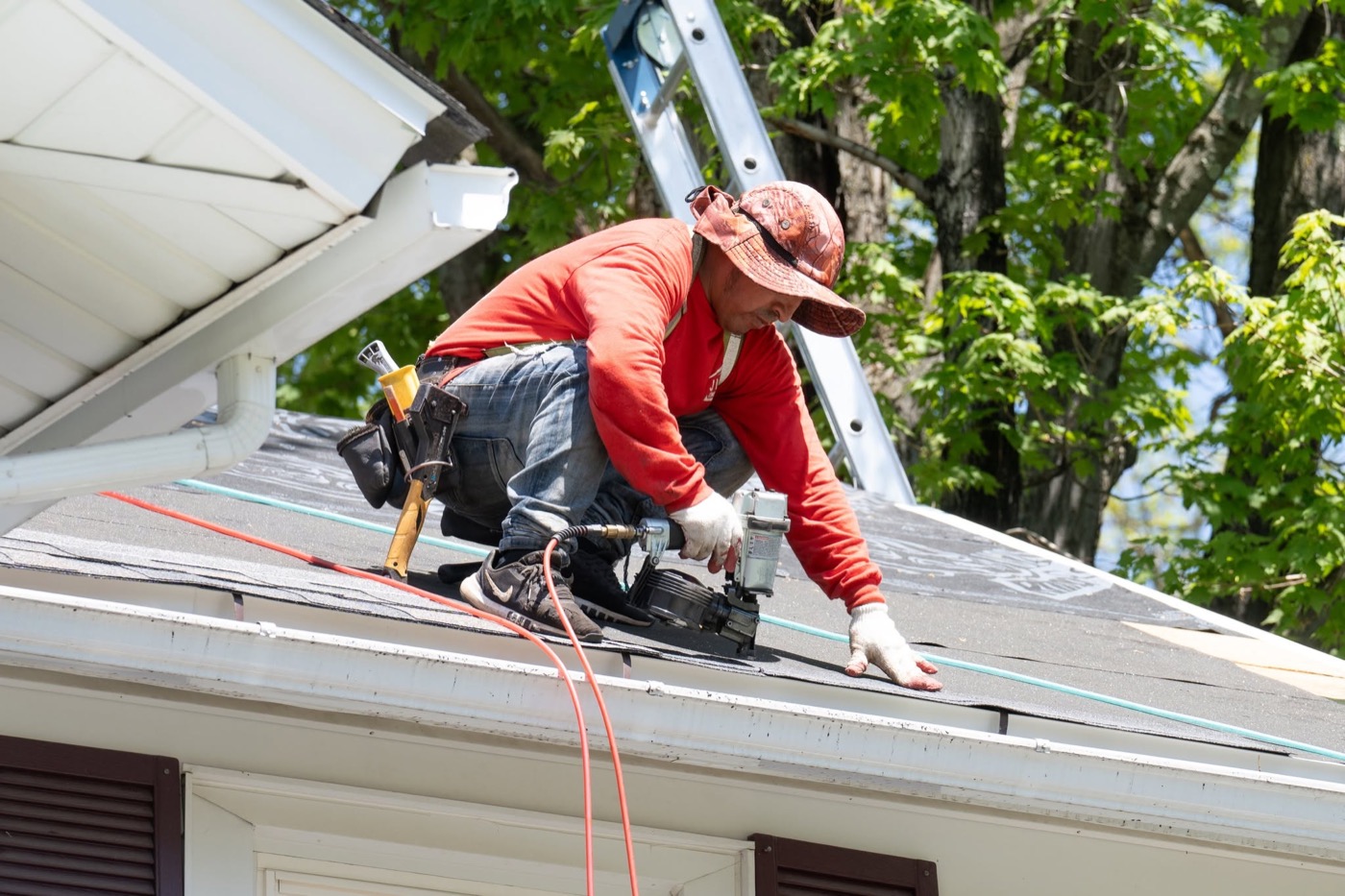 Roofer trimming and refitting shingles at the roof edge during a repair